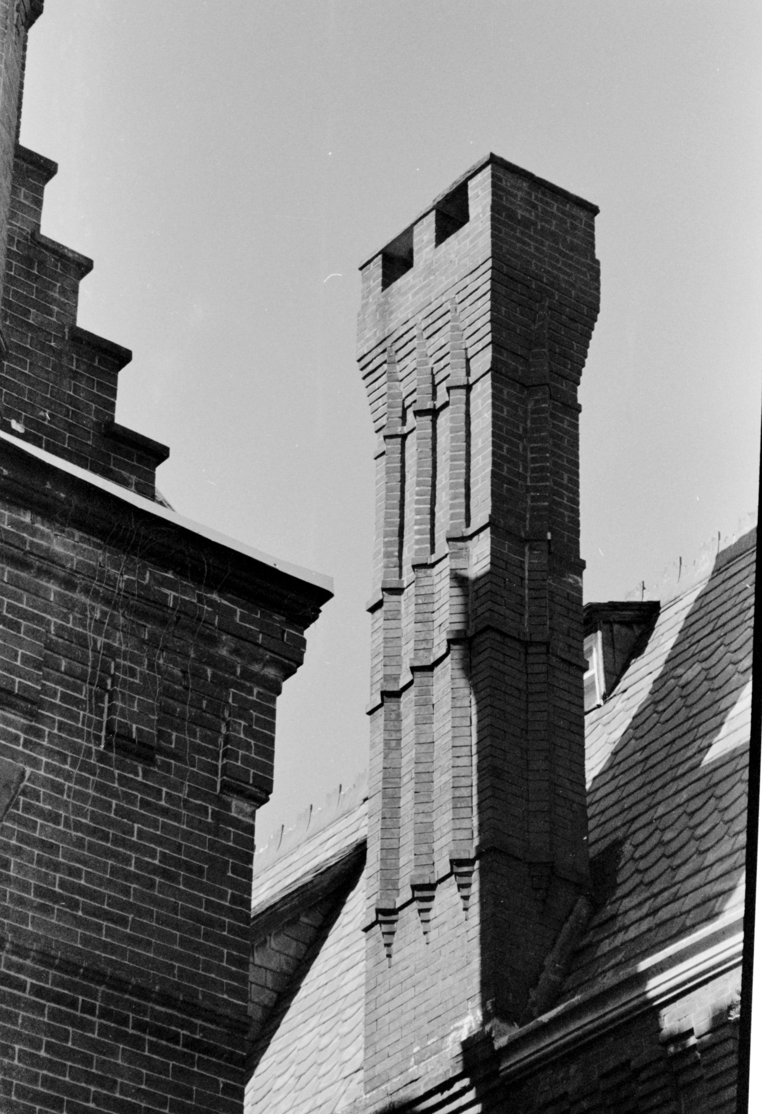 The upper corner of a brick building with a chimney against a clear sky