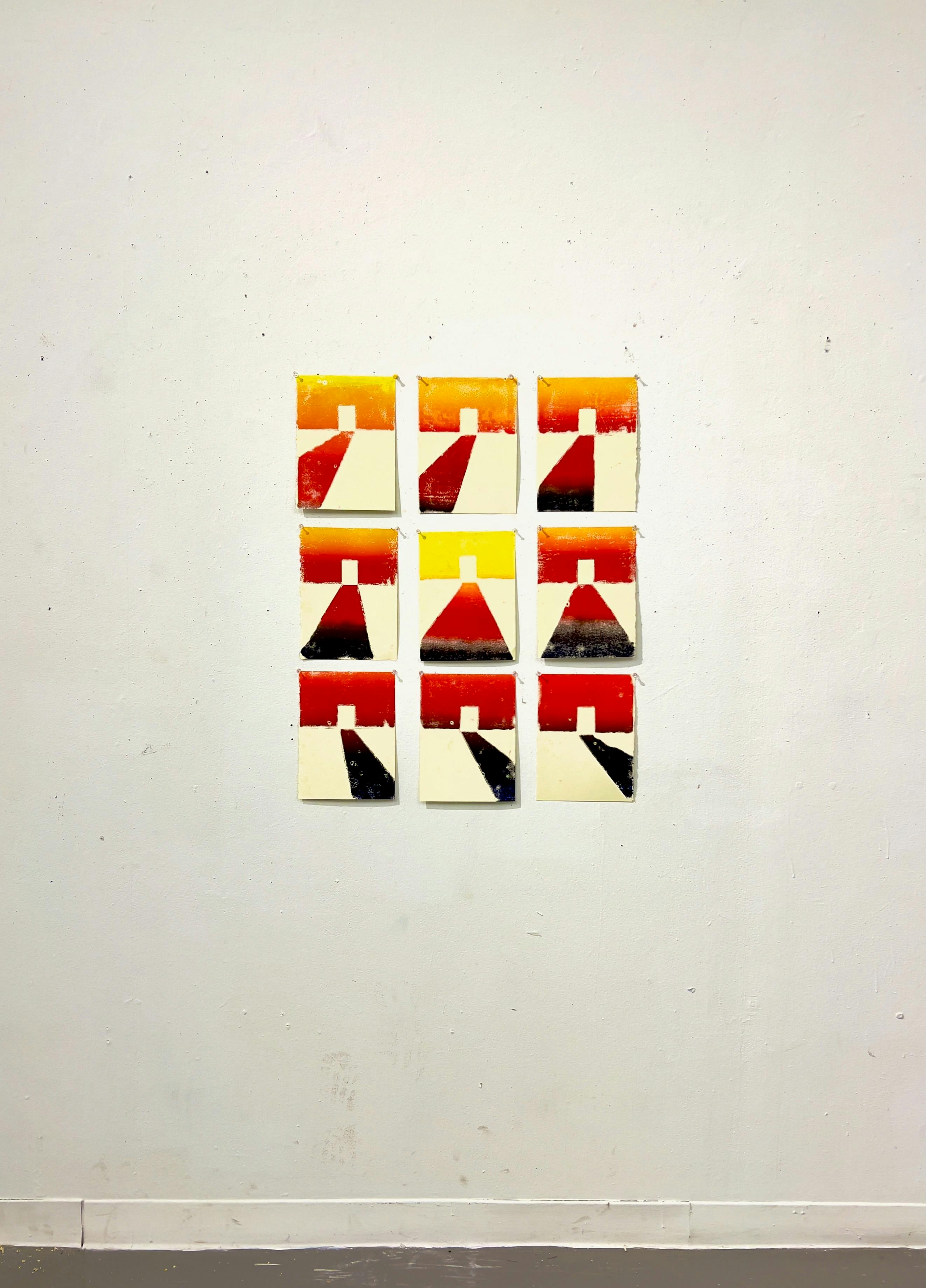 A series of nine monoprints arranged in a 3x3 grid on a white wall. Each print features an abstract doorway with light coming through it. The light is changing in each print, suggesting the passage of time. The color palette includes warm tones of yellow, orange, red, and a dark blue