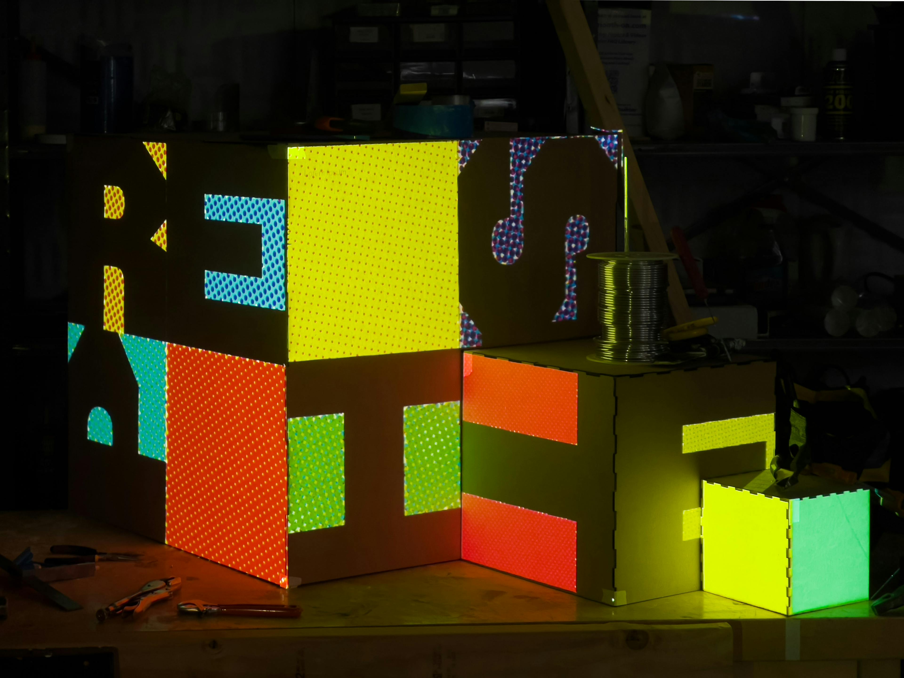Colorful text that reads respite projected onto the three cardboard cubes