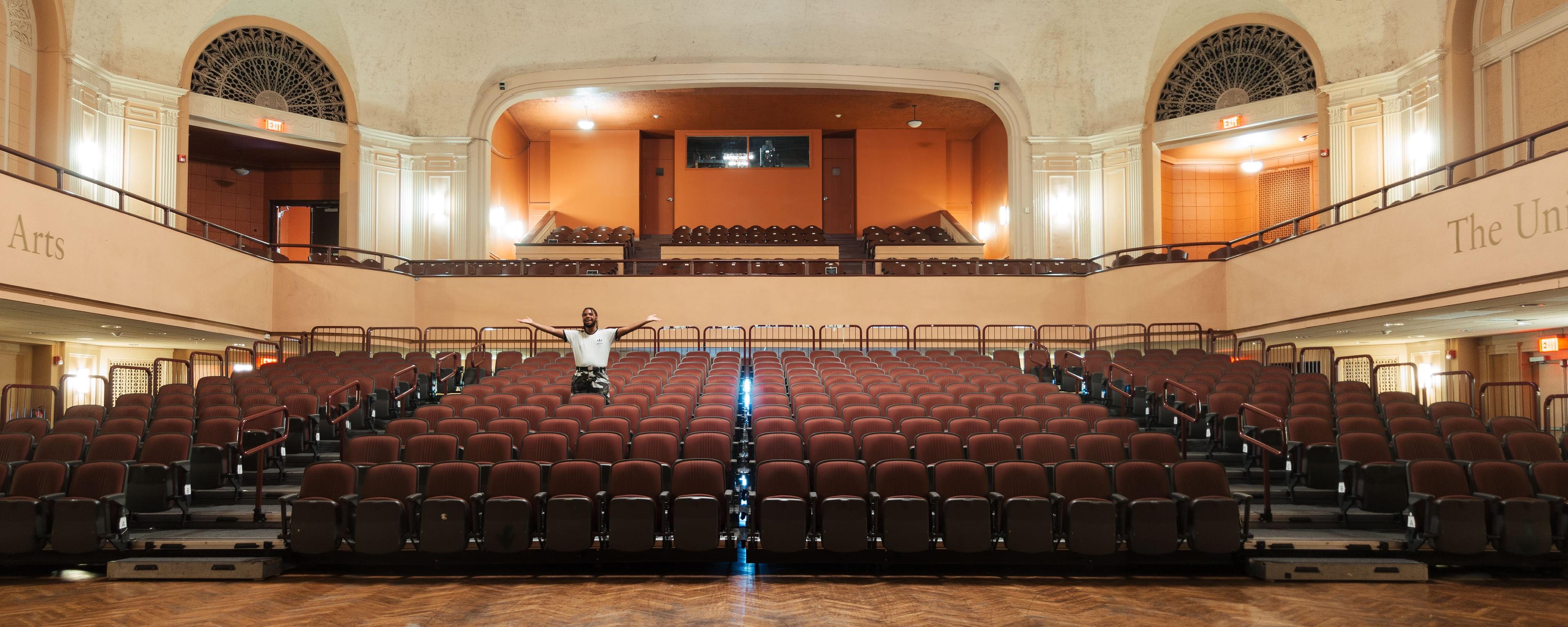 Empty suditorium view from stage with man standing up alone in the seats.