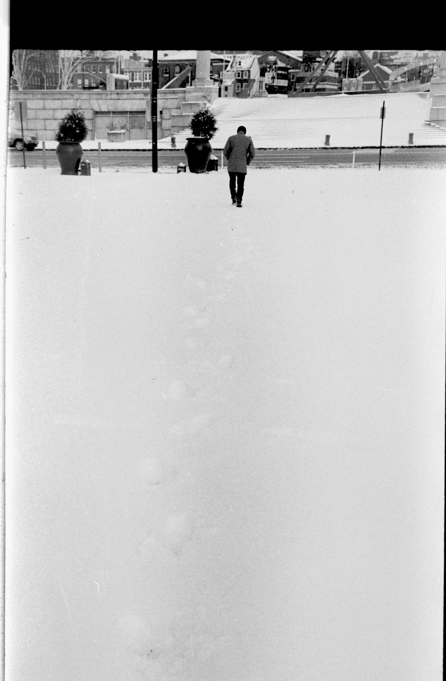 A person walking outdoors in a snowy landscape, carrying a bag and walking away from the viewpoint