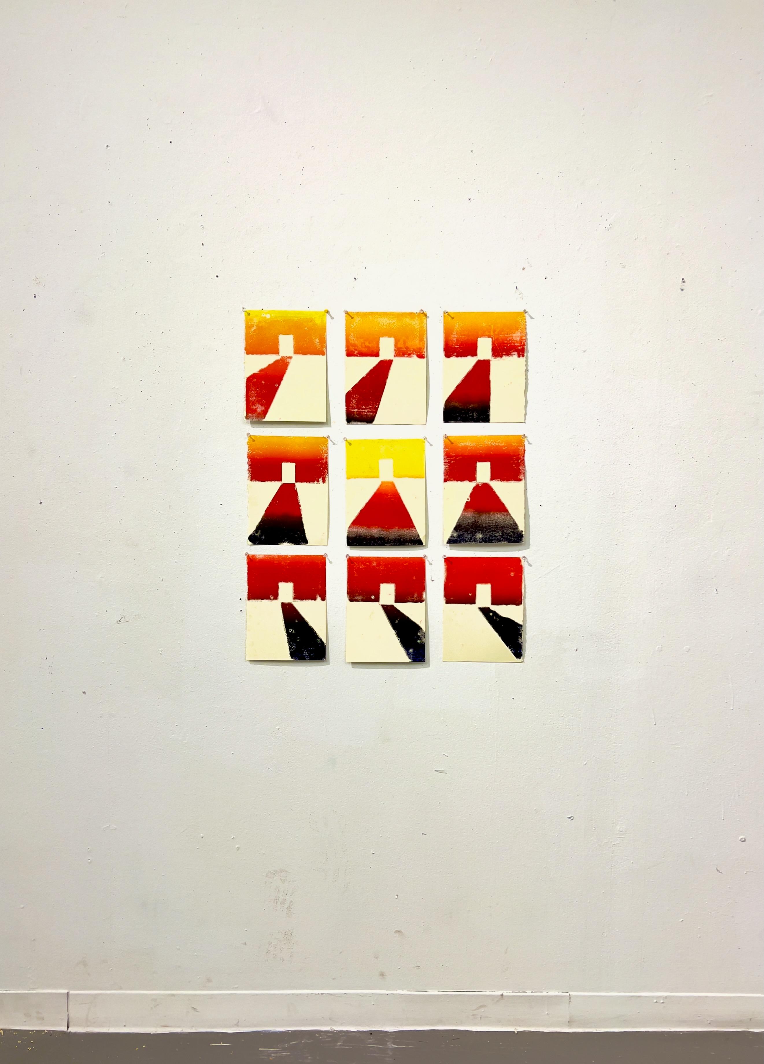 A series of nine monoprints arranged in a 3x3 grid on a white wall. Each print features an abstract doorway with light coming through it. The light is changing in each print, suggesting the passage of time. The color palette includes warm tones of yellow, orange, red, and a dark blue