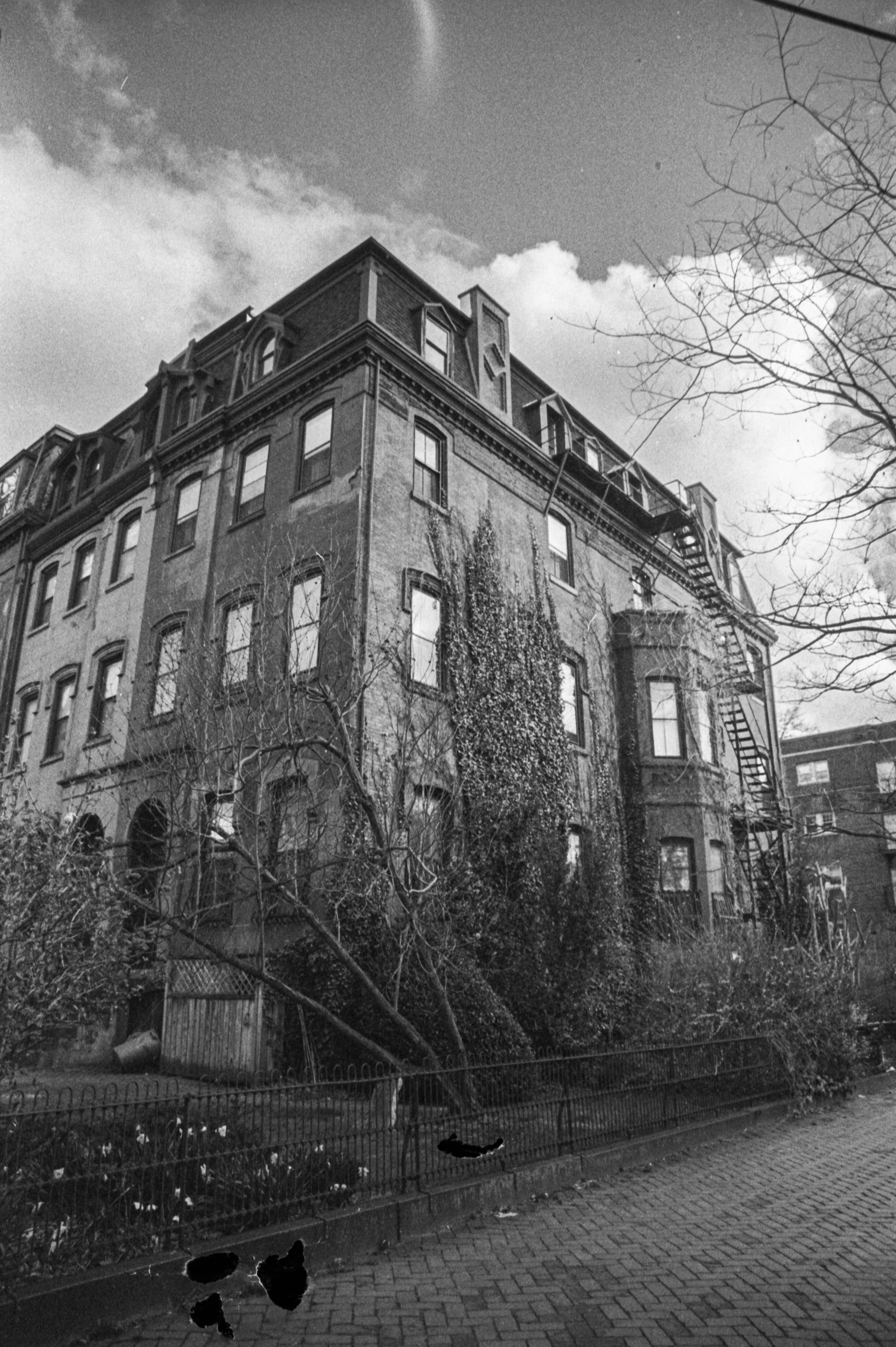 Corner house surrounded by ivy under a partly cloudy sky on Spruce St in Philadelphia